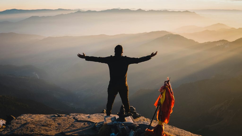 Silhouette of a person standing on a rock with arms stretched open during a scenic sunrise or sunset.